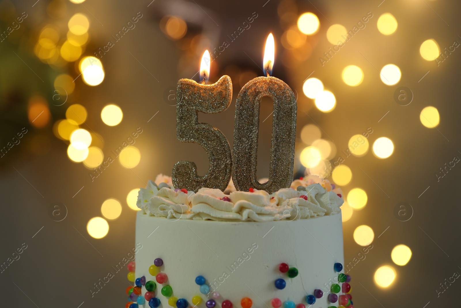 Photo of 50th birthday. Burning number shaped candles on cake against blurred background with lights, closeup. Bokeh effect