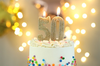 Photo of 50th birthday. Burning number shaped candles on cake against blurred background with lights, closeup. Bokeh effect