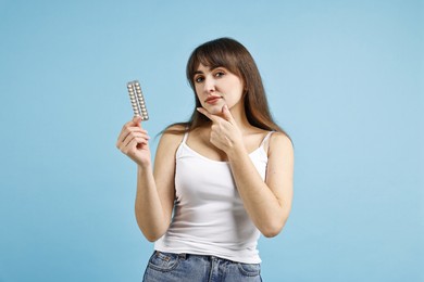 Young woman with blister of contraceptive pills on light blue background