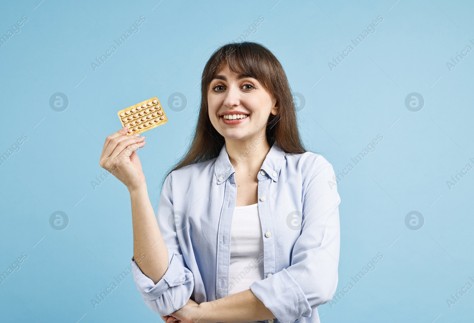 Photo of Smiling woman with blister of contraceptive pills on light blue background