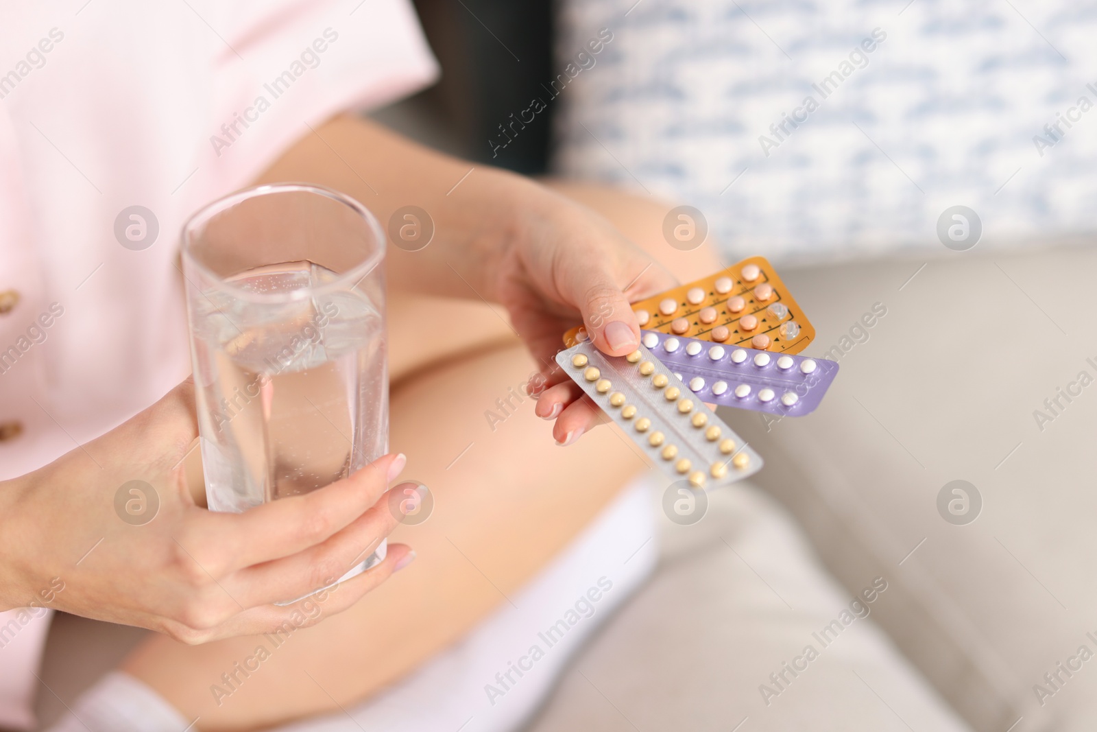 Photo of Woman with contraceptive pills and glass of water on sofa indoors, closeup