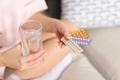 Photo of Woman with contraceptive pills and glass of water on sofa indoors, closeup