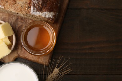 Sweet honey, butter, bread and milk on wooden table, flat lay. Space for text