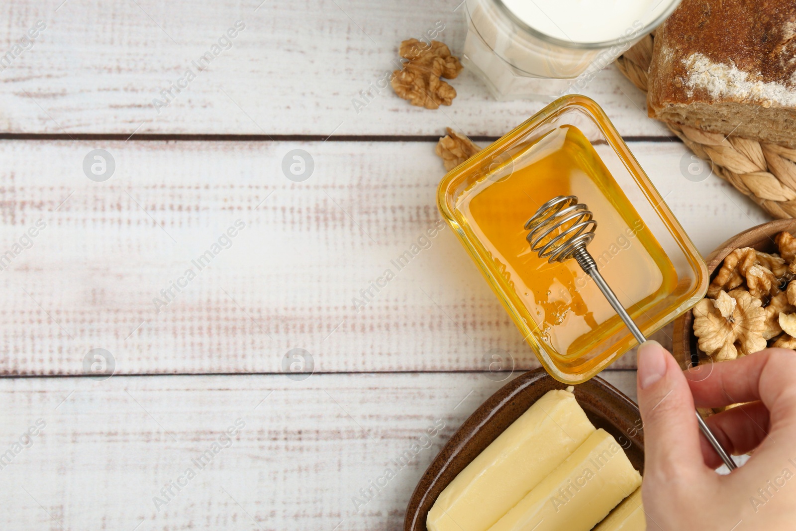 Photo of Woman taking honey with dipper at white wooden table, top view. Space for text