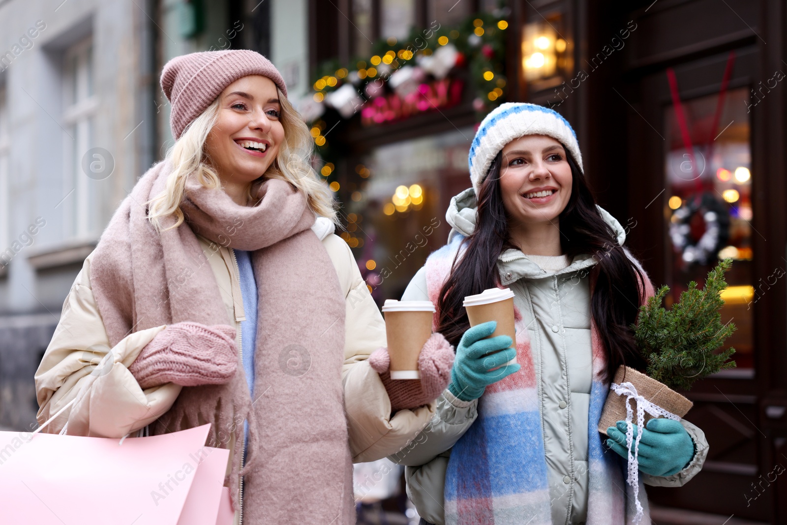 Photo of Happy friends with paper cups of coffee and thuja tree on city street. Christmas season