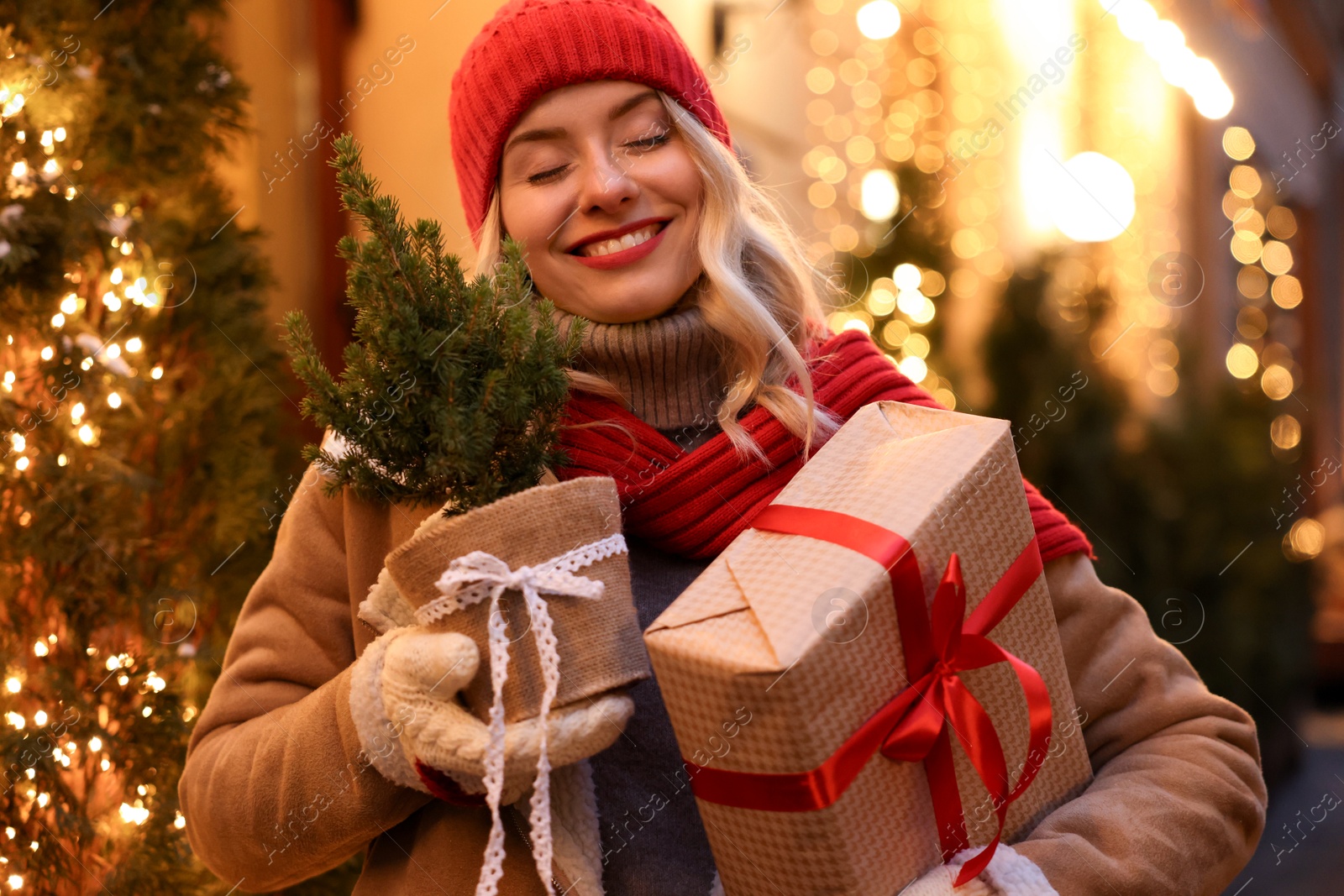 Photo of Happy woman with Christmas gift and thuja tree on city street