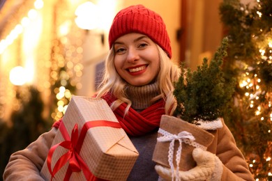 Photo of Happy woman with Christmas gift and thuja tree on city street