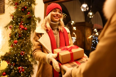 Woman receiving Christmas gifts from friend on city street