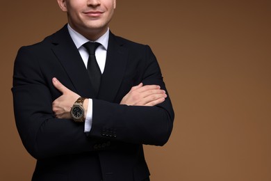 Photo of Man in classic suit with stylish watch on brown background, closeup. Space for text