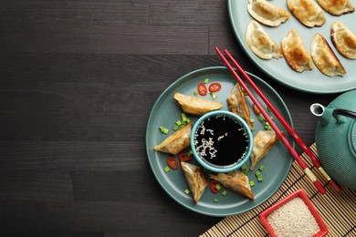 Photo of Delicious fried gyoza dumplings with green onions and chili peppers served on wooden table, flat lay. Space for text