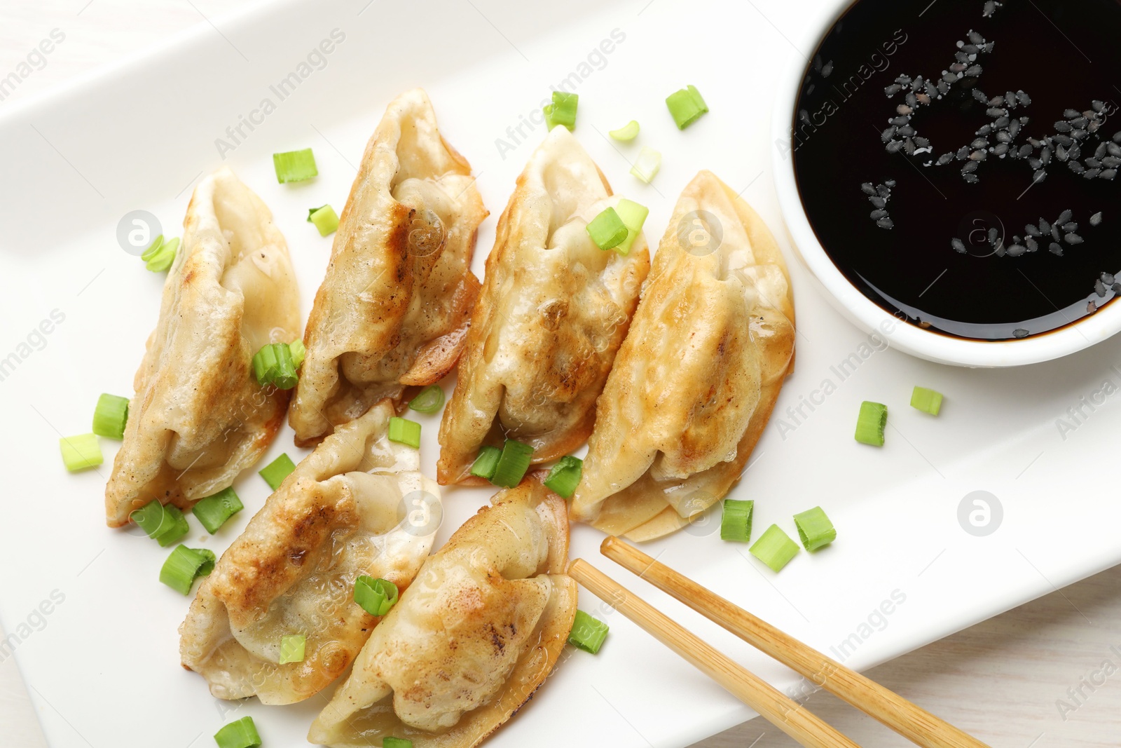 Photo of Fried gyoza dumplings with green onions and soy on white table, closeup