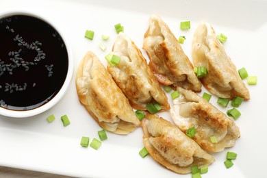 Photo of Fried gyoza dumplings with green onions and soy on table, closeup