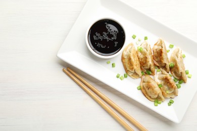 Photo of Delicious fried gyoza dumplings with green onions served on white wooden table, top view. Space for text