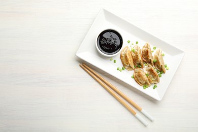 Photo of Delicious fried gyoza dumplings with green onions served on white wooden table, top view. Space for text