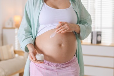 Photo of Pregnant woman applying cream on belly at home, closeup