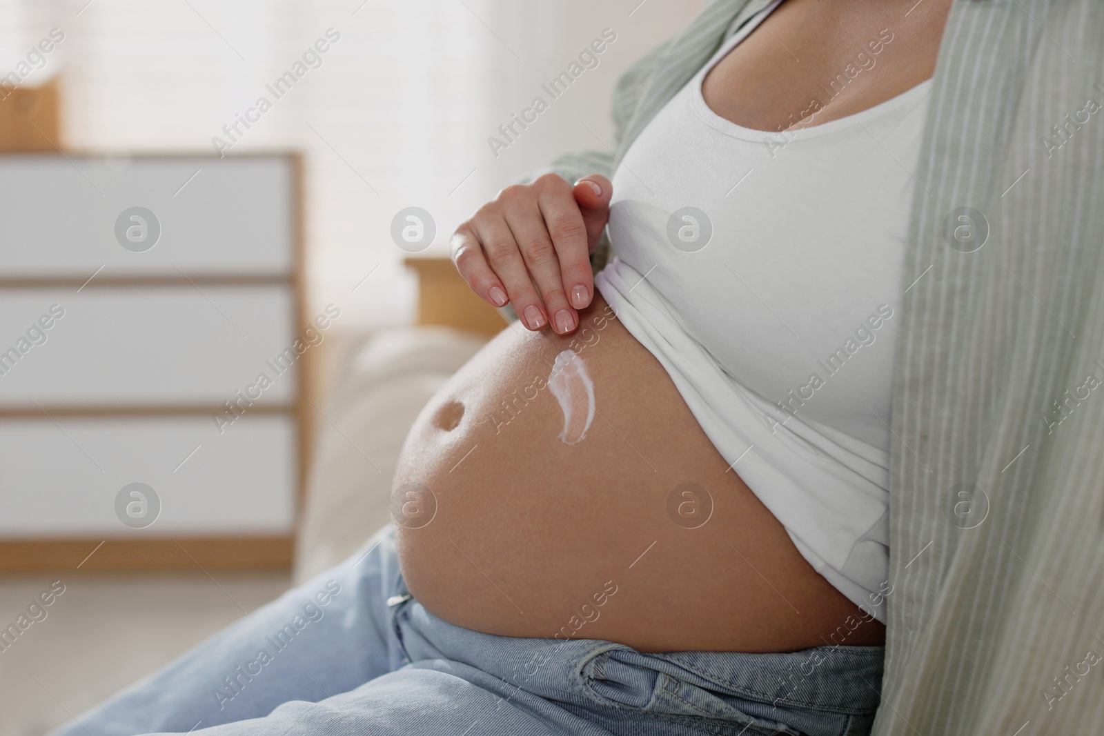 Photo of Pregnant woman applying cream on belly at home, closeup