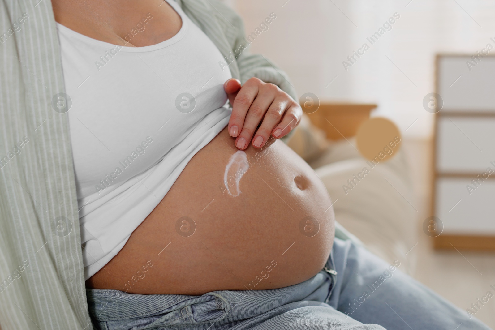 Photo of Pregnant woman applying cream on belly at home, closeup