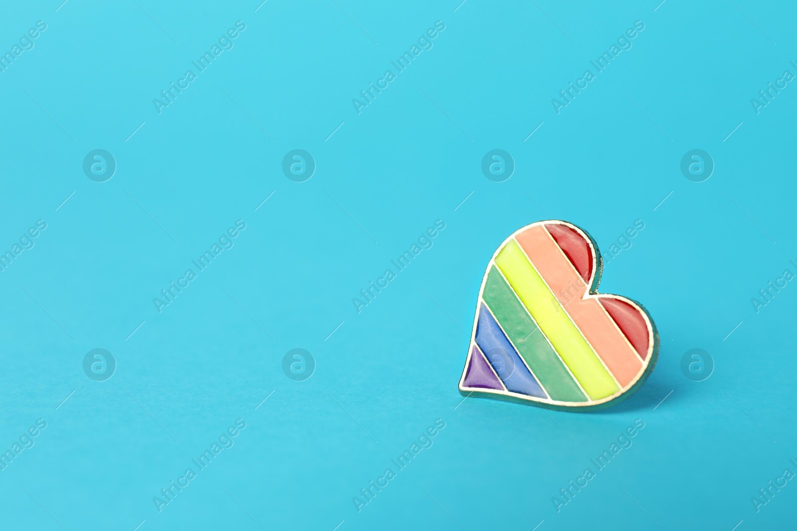 Photo of Heart shaped badge in LGBT colors on light blue background, space for text