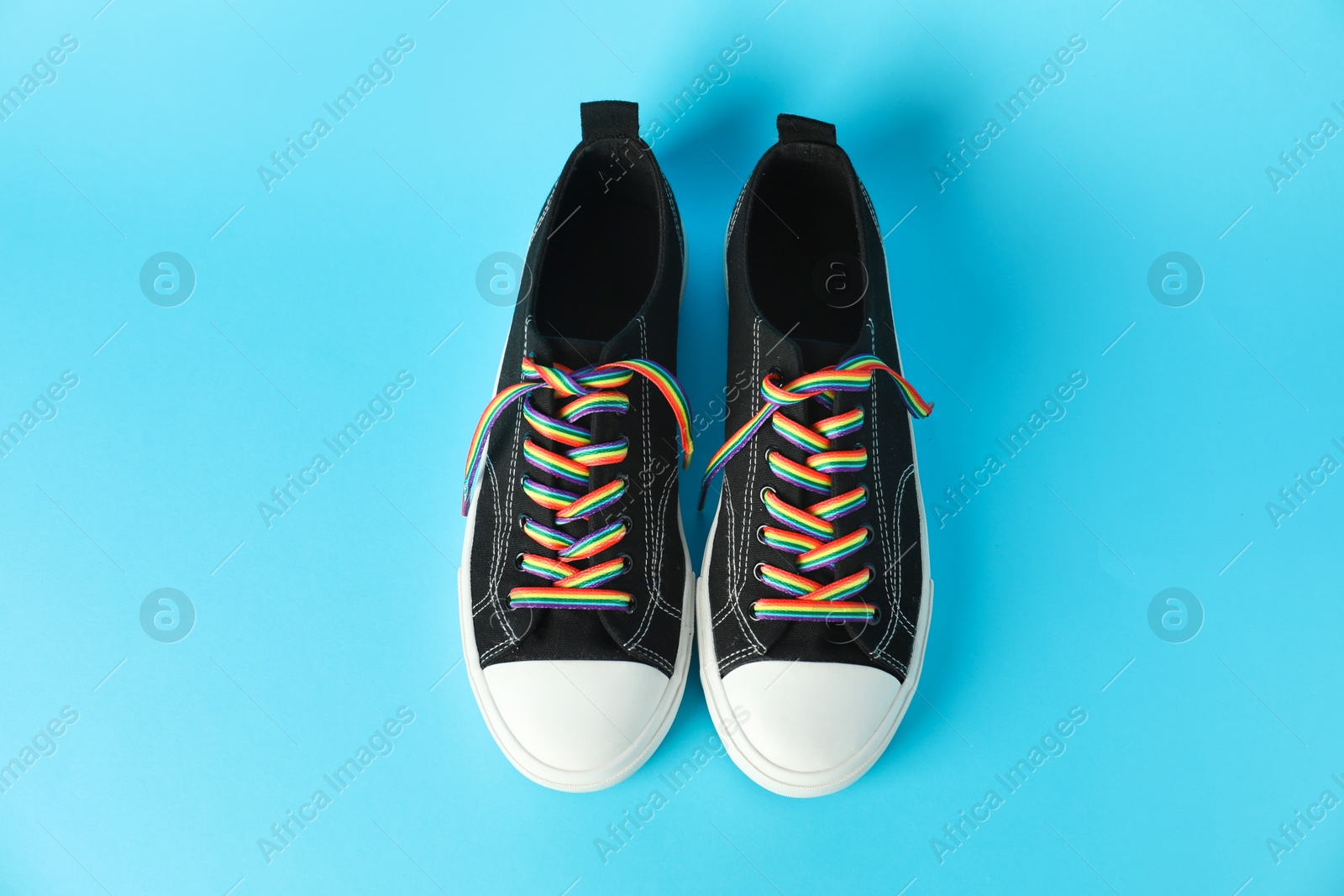 Photo of Black shoes with bright rainbow laces on light blue background, above view. LGBT concept