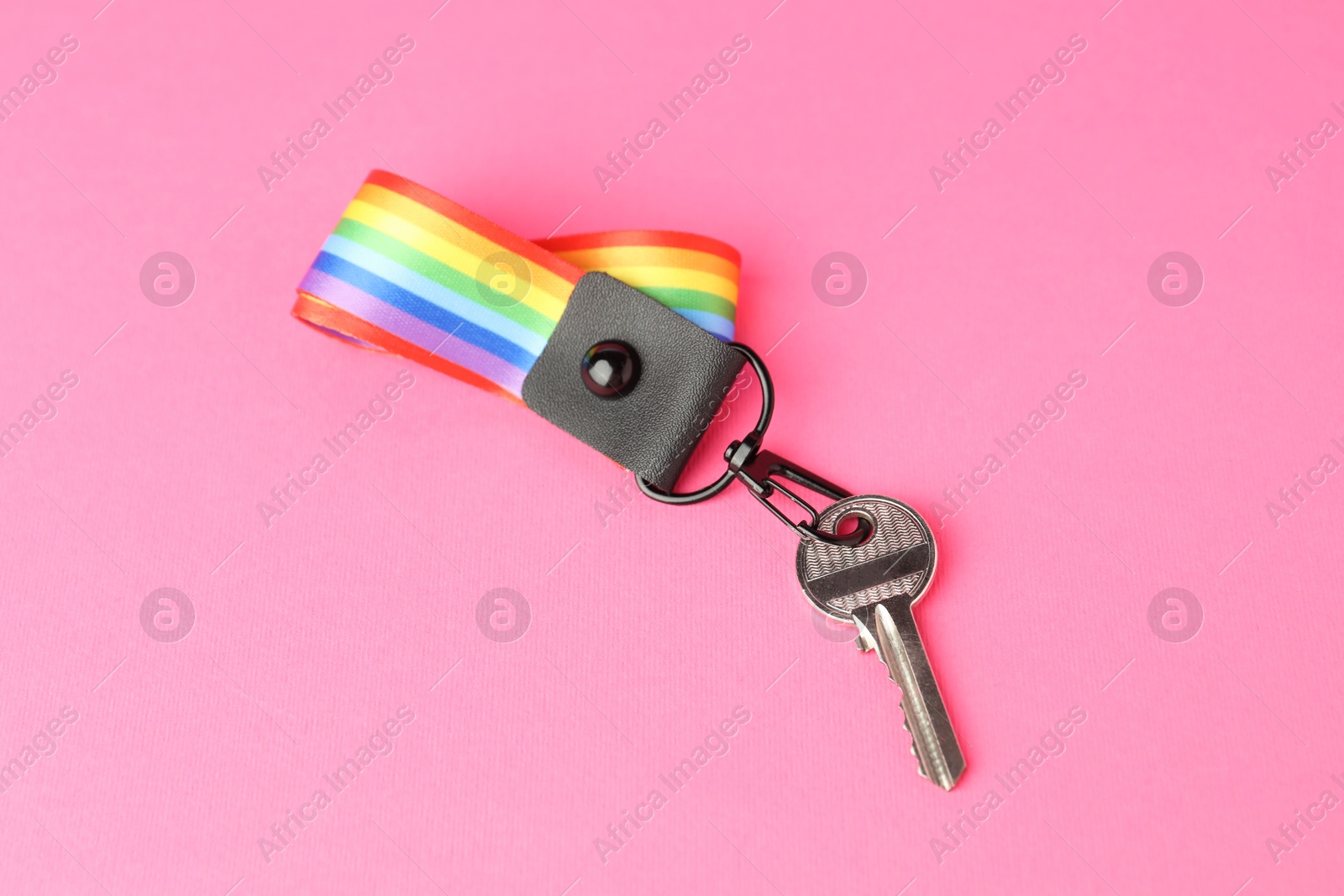 Photo of Key with keychain in LGBT colors on pink background, above view