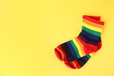 Photo of Pair of socks in LGBT colors on yellow background, top view. Space for text