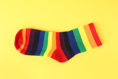 Photo of One sock in LGBT colors on yellow background, top view