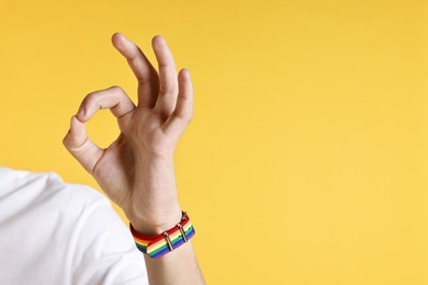 Photo of Man with bracelet in colors of LGBT flag showing okay gesture on yellow background, closeup. Space for text