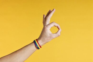 Photo of Man with bracelet in colors of LGBT flag showing okay gesture on yellow background, closeup