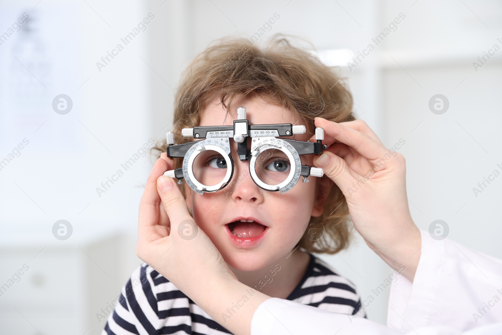 Photo of Ophthalmologist examining little boy's vision with trial frame in clinic, closeup