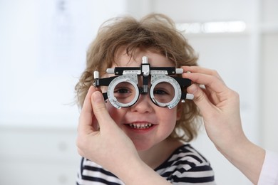 Photo of Ophthalmologist examining little boy's vision with trial frame in clinic, closeup