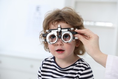 Photo of Ophthalmologist examining little boy's vision with trial frame in clinic, closeup