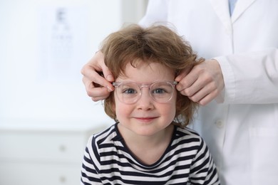 Photo of Vision testing. Ophthalmologist giving glasses to little boy in clinic, closeup