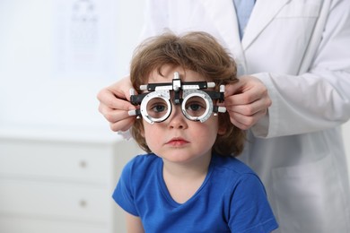 Ophthalmologist examining little boy's vision with trial frame in clinic, closeup