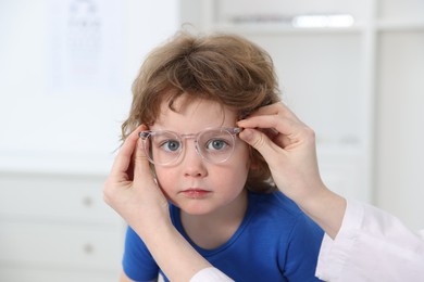 Vision testing. Ophthalmologist giving glasses to little boy in clinic, closeup