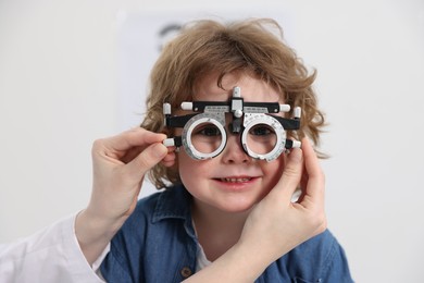 Photo of Ophthalmologist examining little boy's vision with trial frame in clinic, closeup