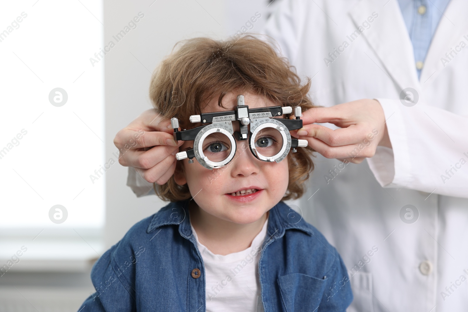 Photo of Ophthalmologist examining little boy's vision with trial frame in clinic, closeup