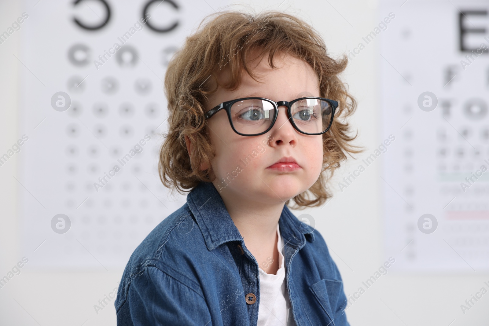 Photo of Little boy wearing glasses near vision test chart at ophthalmologist office