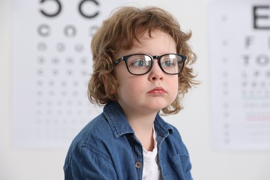 Little boy wearing glasses near vision test chart at ophthalmologist office