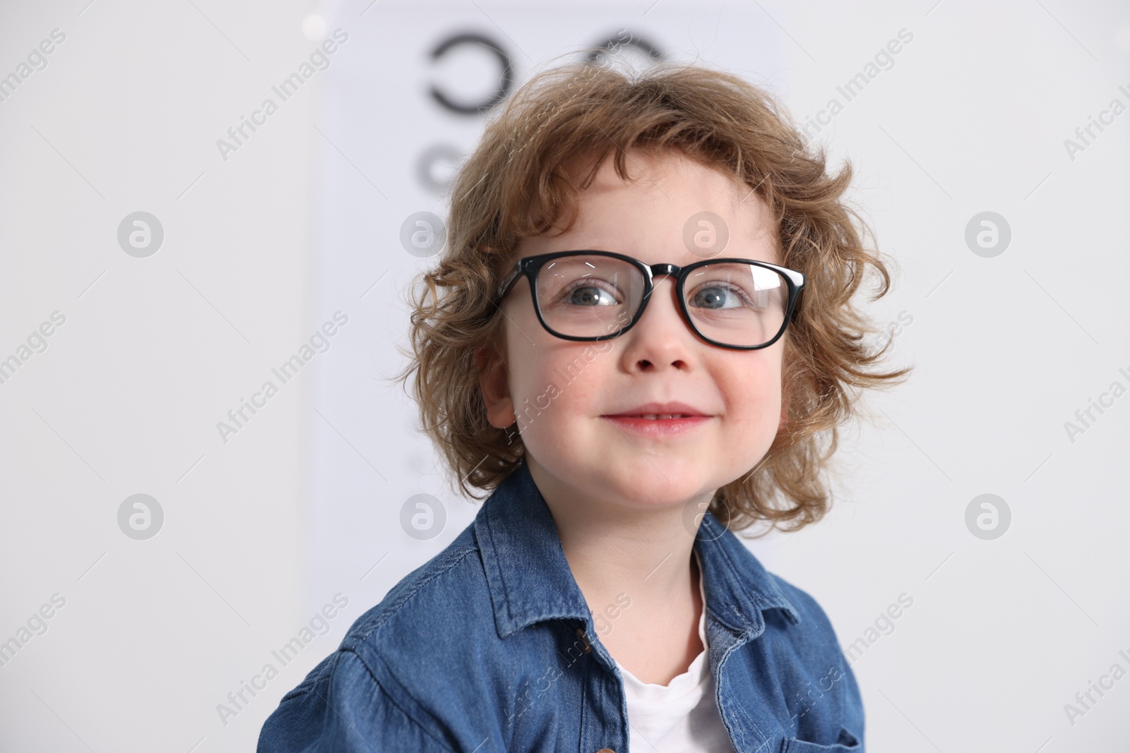 Photo of Little boy wearing glasses near vision test chart at ophthalmologist office