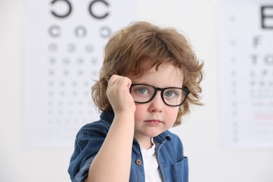 Photo of Little boy wearing glasses near vision test chart at ophthalmologist office