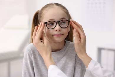 Photo of Vision testing. Ophthalmologist giving glasses to little girl in clinic, closeup