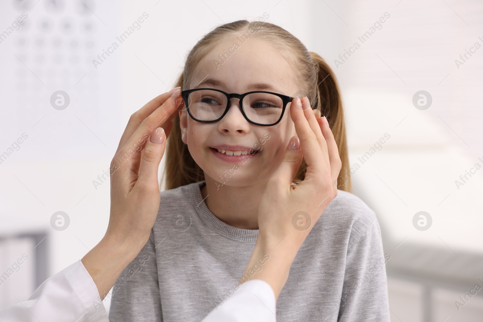 Photo of Vision testing. Ophthalmologist giving glasses to little girl in clinic, closeup