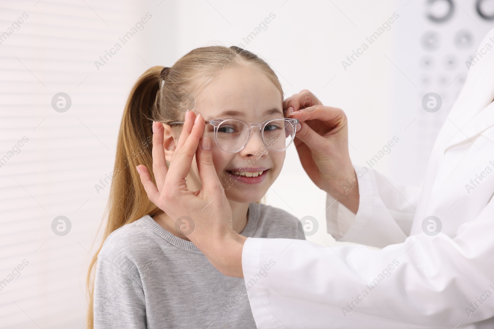 Photo of Vision testing. Ophthalmologist giving glasses to little girl in clinic, closeup