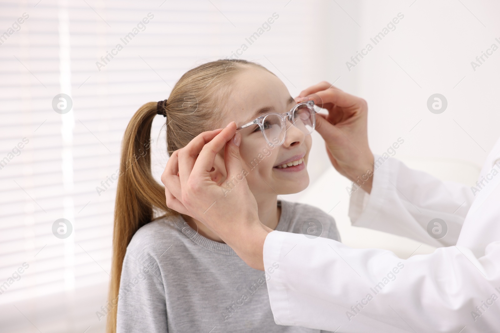 Photo of Vision testing. Ophthalmologist giving glasses to little girl in clinic, closeup