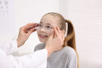 Photo of Vision testing. Ophthalmologist giving glasses to little girl in clinic, closeup