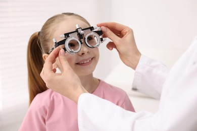 Photo of Ophthalmologist examining girl's vision with trial frame in clinic, closeup