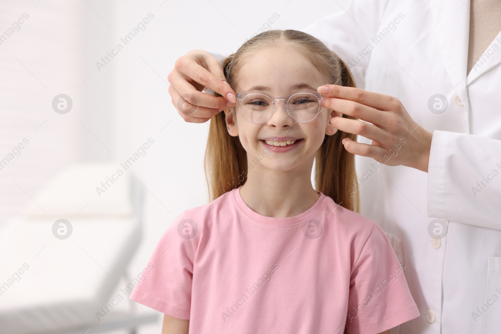 Photo of Vision testing. Ophthalmologist giving glasses to little girl in clinic, closeup