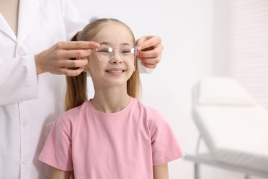 Photo of Vision testing. Ophthalmologist giving glasses to little girl in clinic, closeup