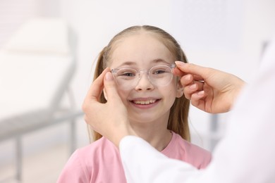 Photo of Vision testing. Ophthalmologist giving glasses to little girl in clinic, closeup