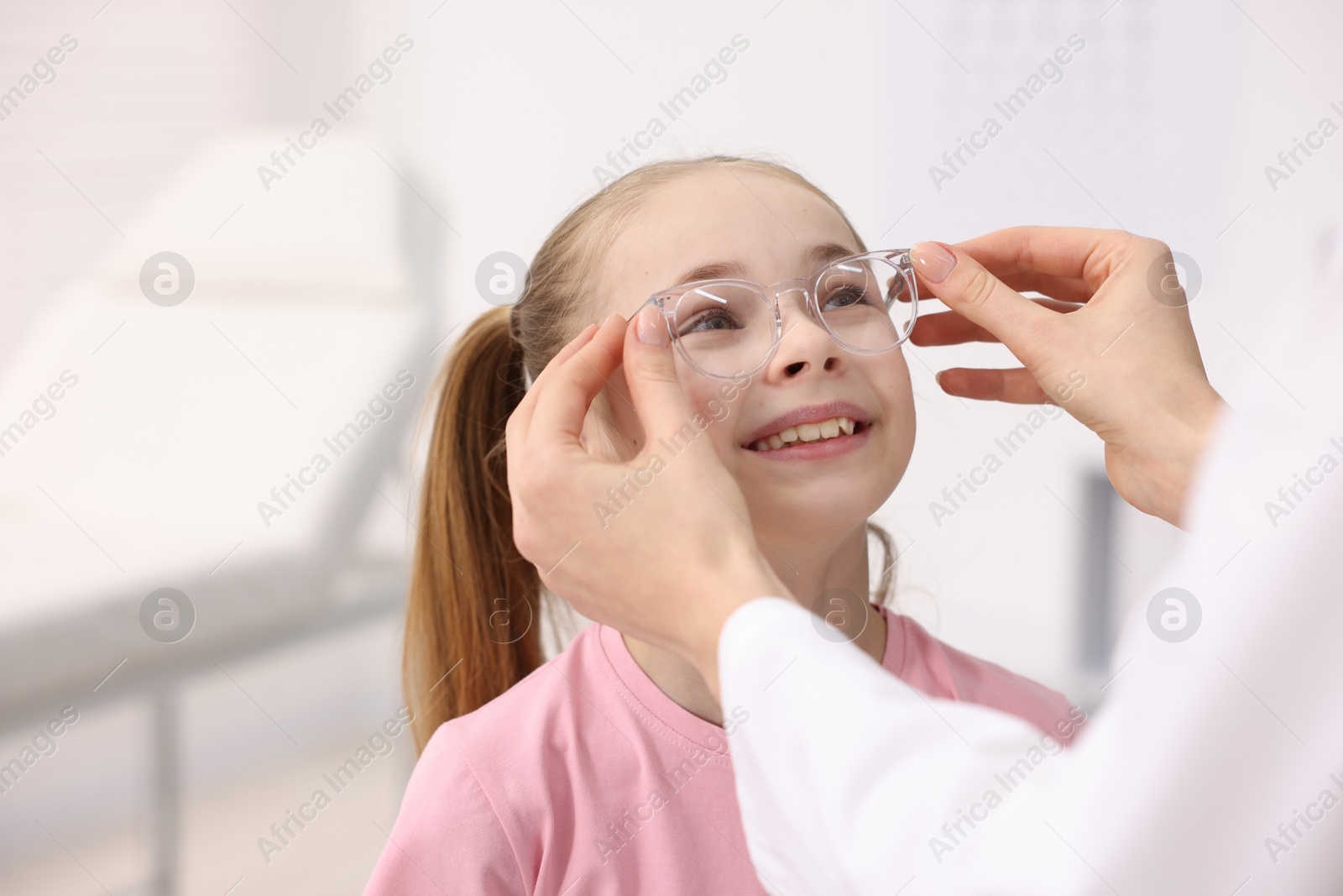 Photo of Vision testing. Ophthalmologist giving glasses to little girl in clinic, closeup